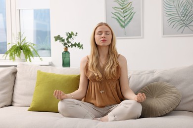 Photo of Feng shui. Young woman meditating on couch at home