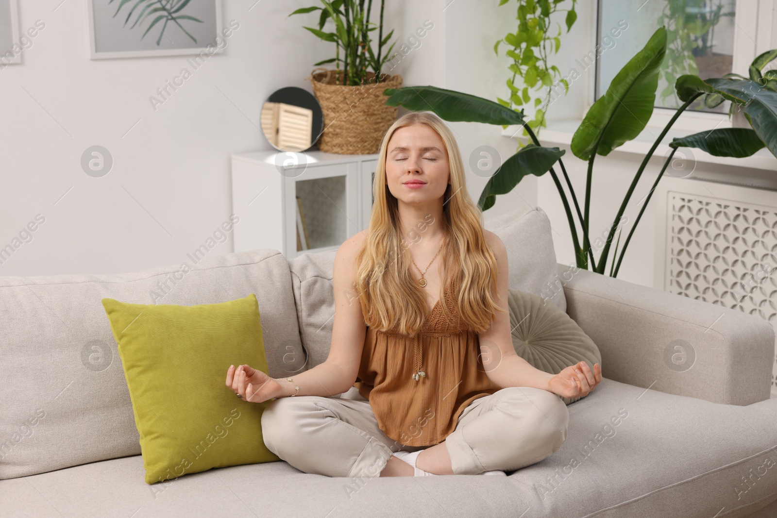 Photo of Feng shui. Young woman meditating on couch at home