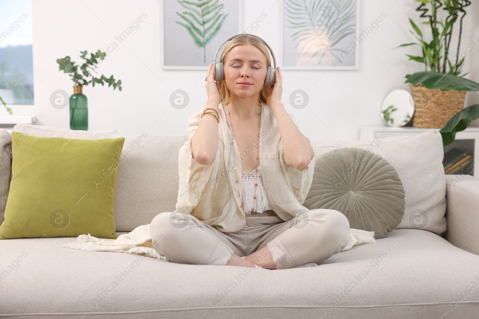 Photo of Feng shui. Young woman with headphones meditating on couch at home