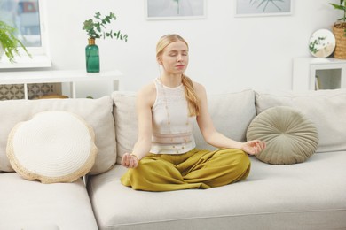 Feng shui. Young woman meditating on couch at home