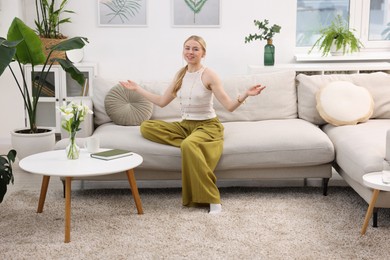 Photo of Feng shui. Young woman meditating on couch at home