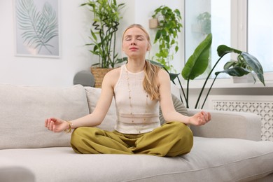 Photo of Feng shui. Young woman meditating on couch at home