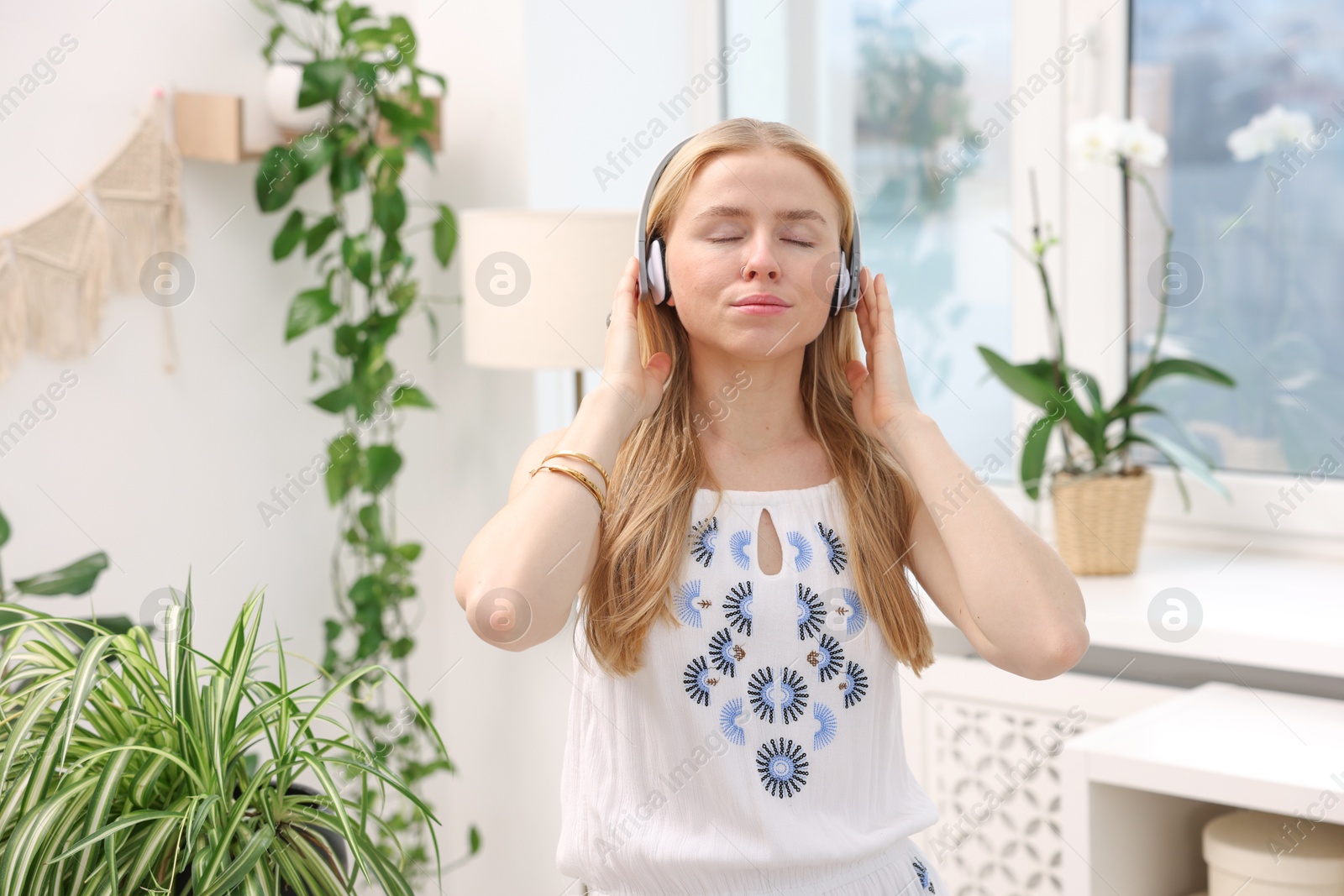 Photo of Feng shui. Young woman in headphones listening to music near houseplants at home