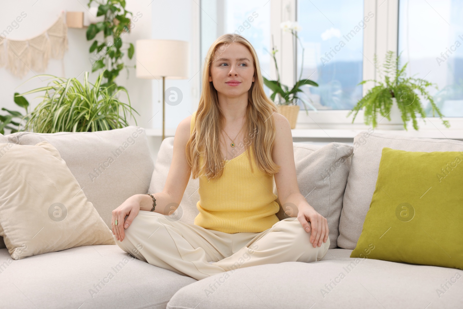 Photo of Feng shui. Young woman meditating on couch at home