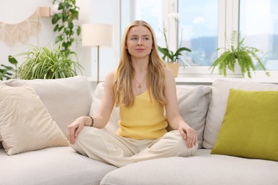 Photo of Feng shui. Young woman meditating on couch at home