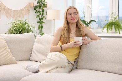 Photo of Feng shui. Young woman with cup of drink sitting on couch at home