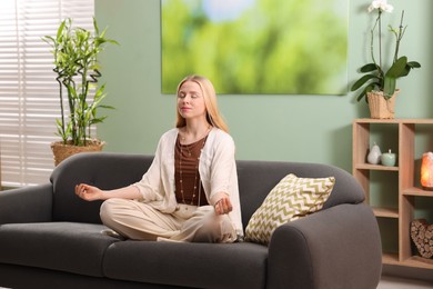 Photo of Feng shui. Young woman meditating on couch at home''