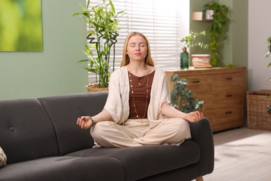 Photo of Feng shui. Young woman meditating on couch at home''