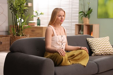 Feng shui. Young woman meditating on couch at home''