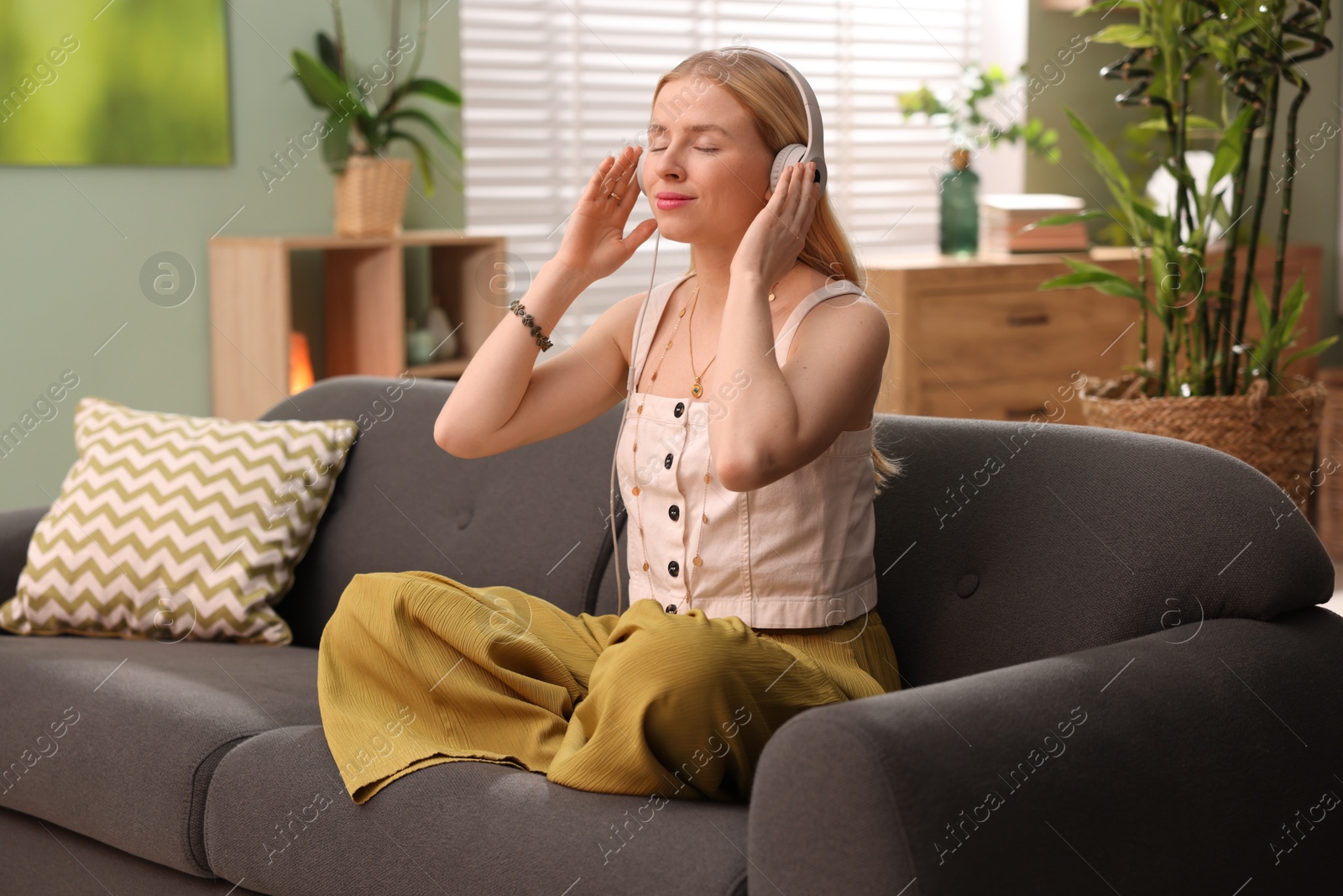 Photo of Feng shui. Young woman with headphones meditating on couch at home''