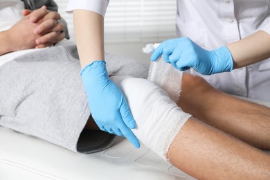 Photo of Doctor bandaging patient's knee in clinic, closeup