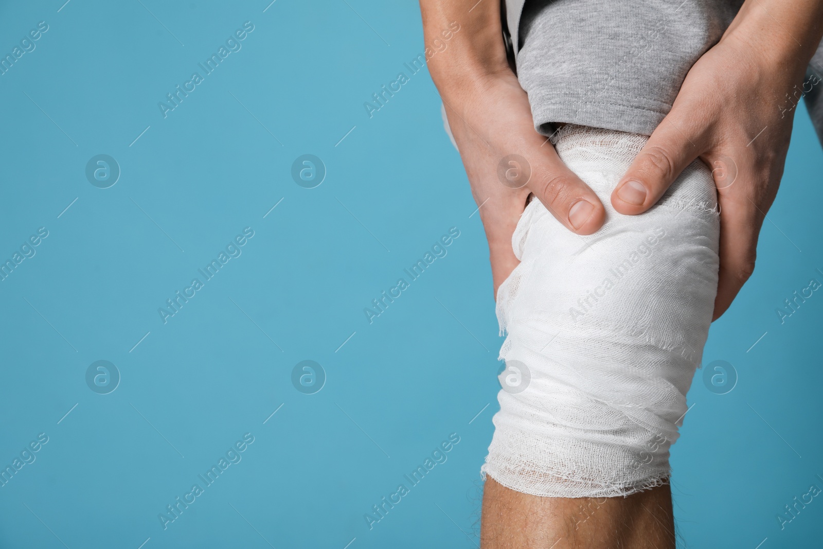 Photo of Man with medical bandage on his knee against light blue background, closeup. Space for text