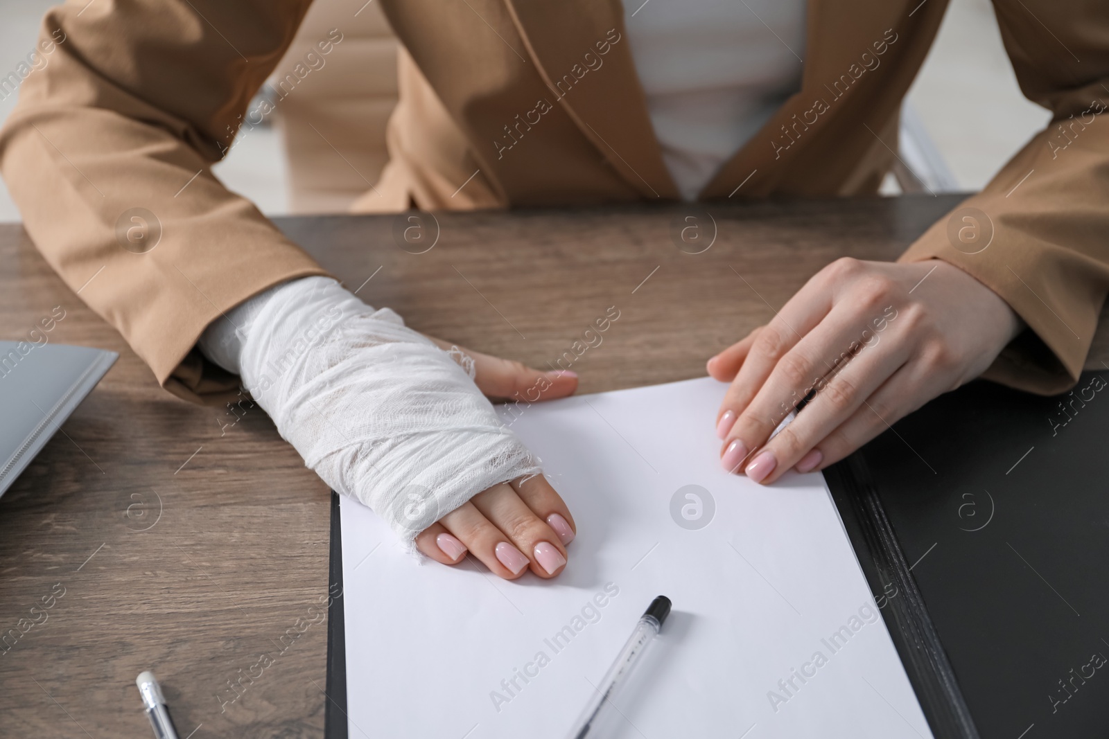 Photo of Woman with medical bandage on her wrist working at wooden table indoors, closeup