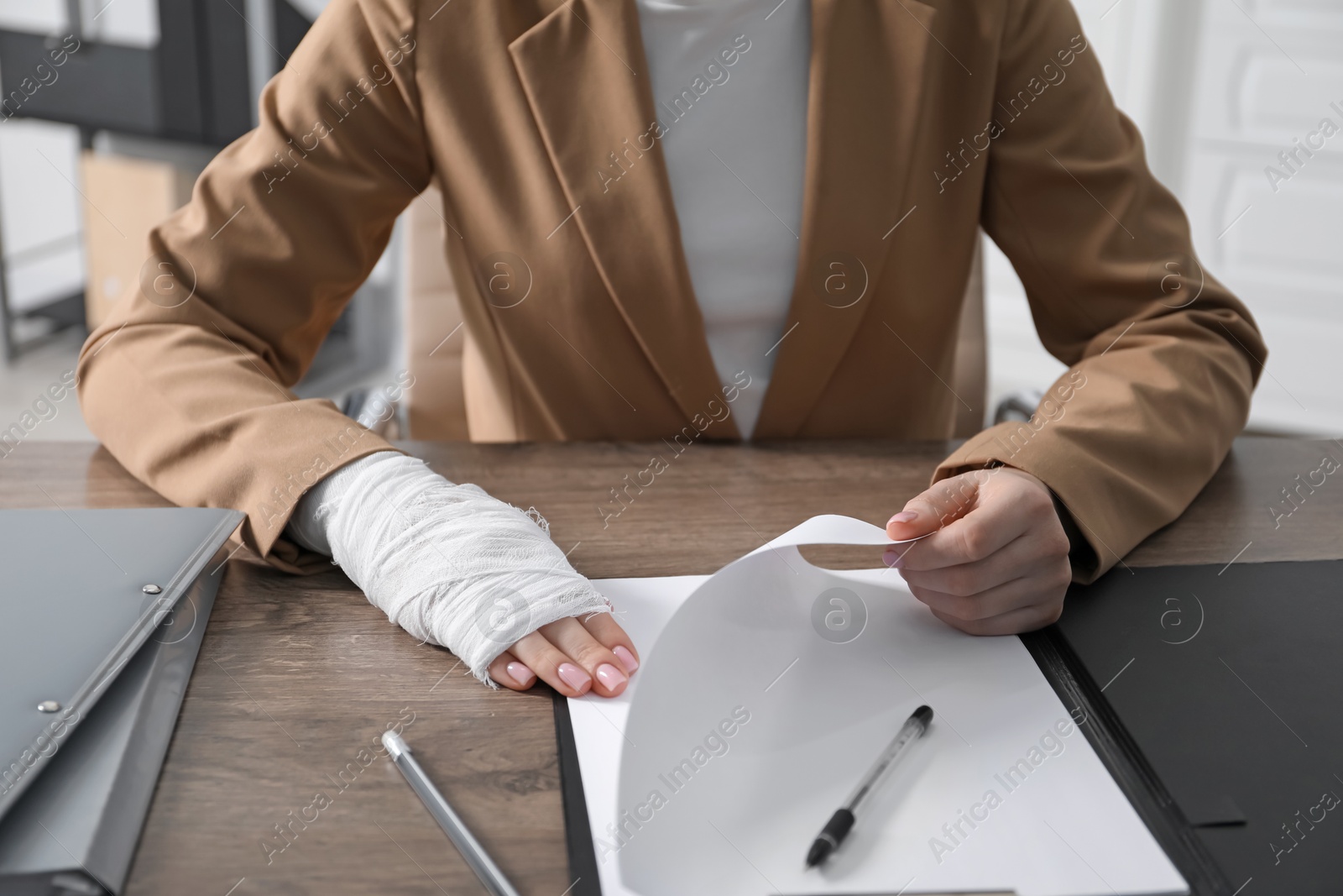 Photo of Woman with medical bandage on her wrist working at wooden table indoors, closeup