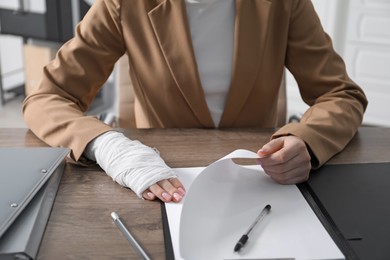 Photo of Woman with medical bandage on her wrist working at wooden table indoors, closeup