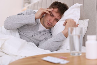 Photo of Unhappy young man suffering from hangover on bed at home