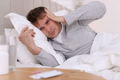 Photo of Unhappy young man suffering from hangover on bed at home