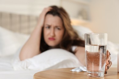 Unhappy woman with glass of water suffering from hangover on bed at home, selective focus