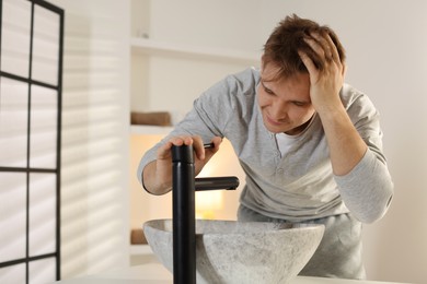 Photo of Unhappy young man suffering from hangover near sink in bathroom