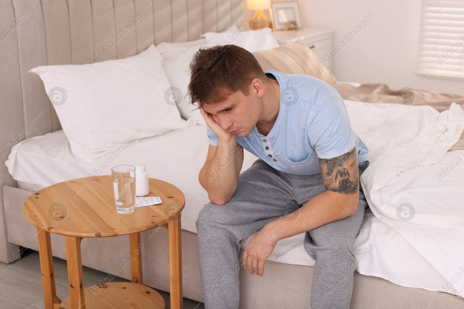 Photo of Unhappy young man suffering from hangover on bed at home