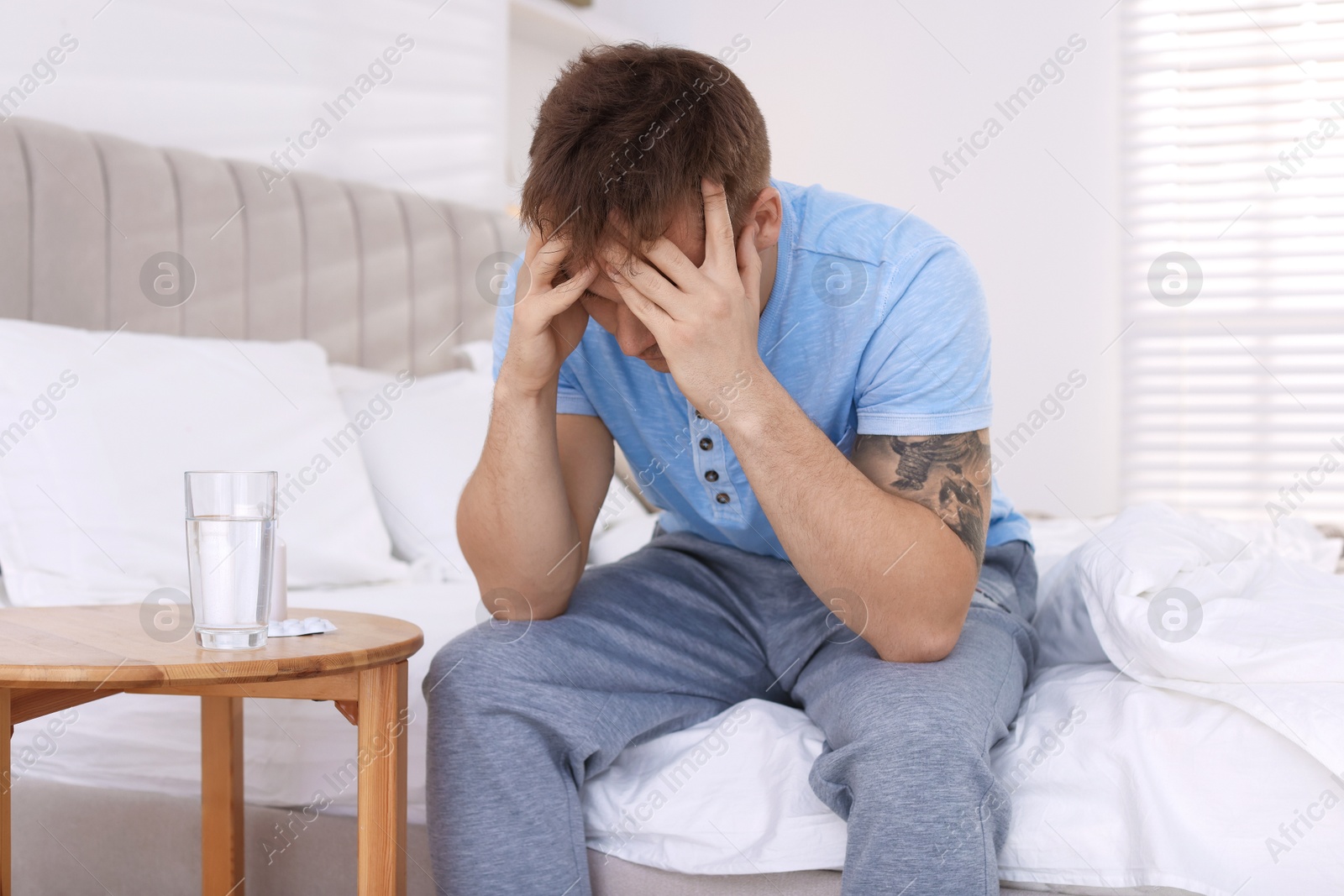 Photo of Unhappy young man suffering from hangover on bed at home