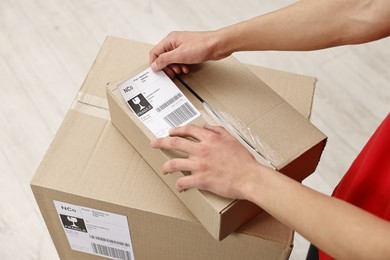 Man sticking shipping label with barcode on parcel indoors, closeup