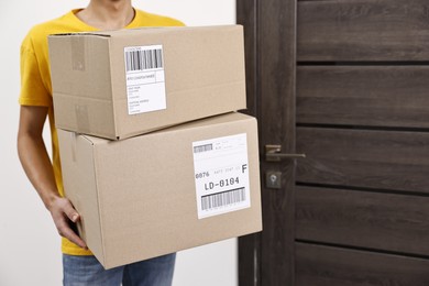 Photo of Man holding parcels with shipping labels near door indoors, closeup. Space for text