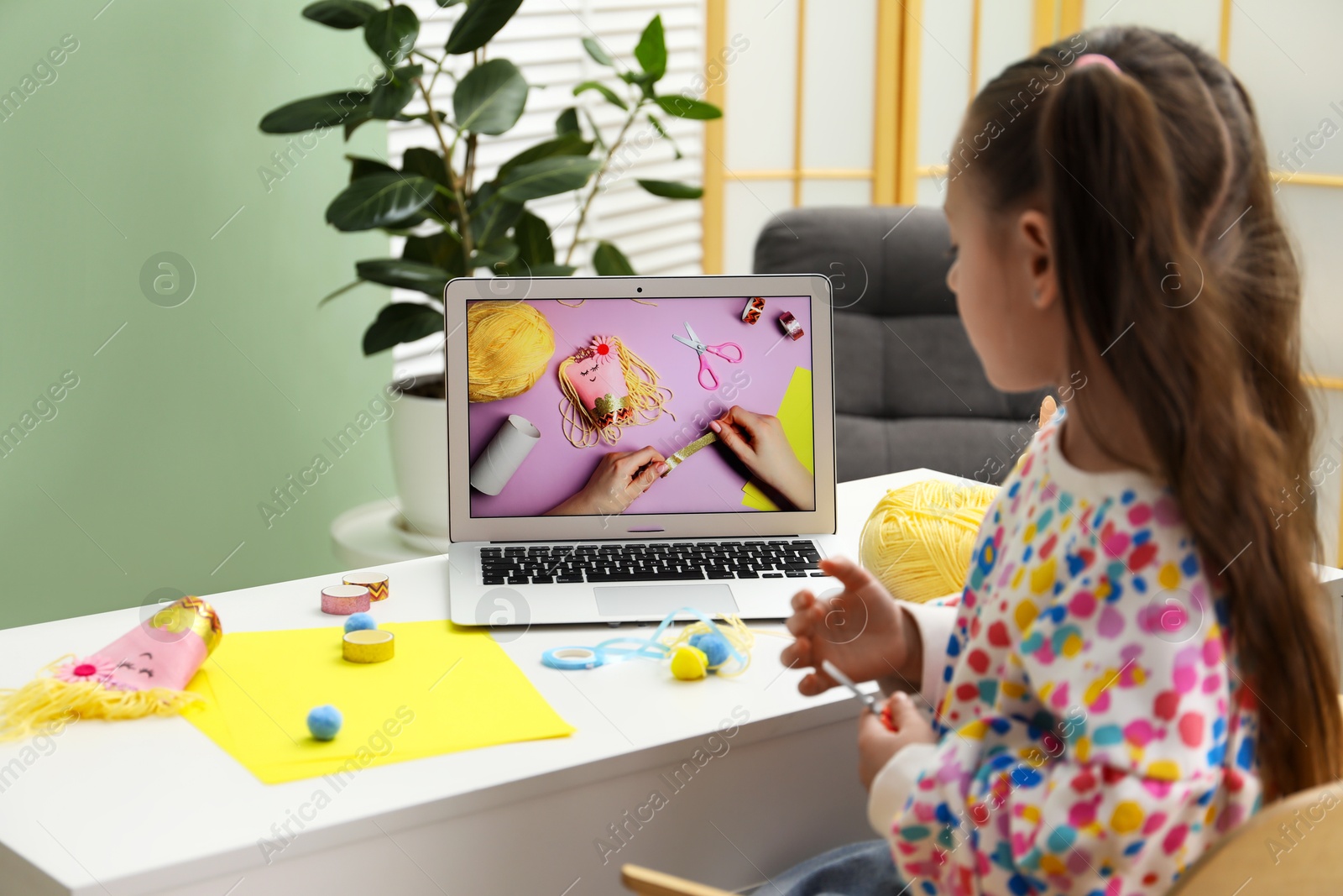 Photo of Little girl making handmade toy by following craft tutorial video at home. Child creativity