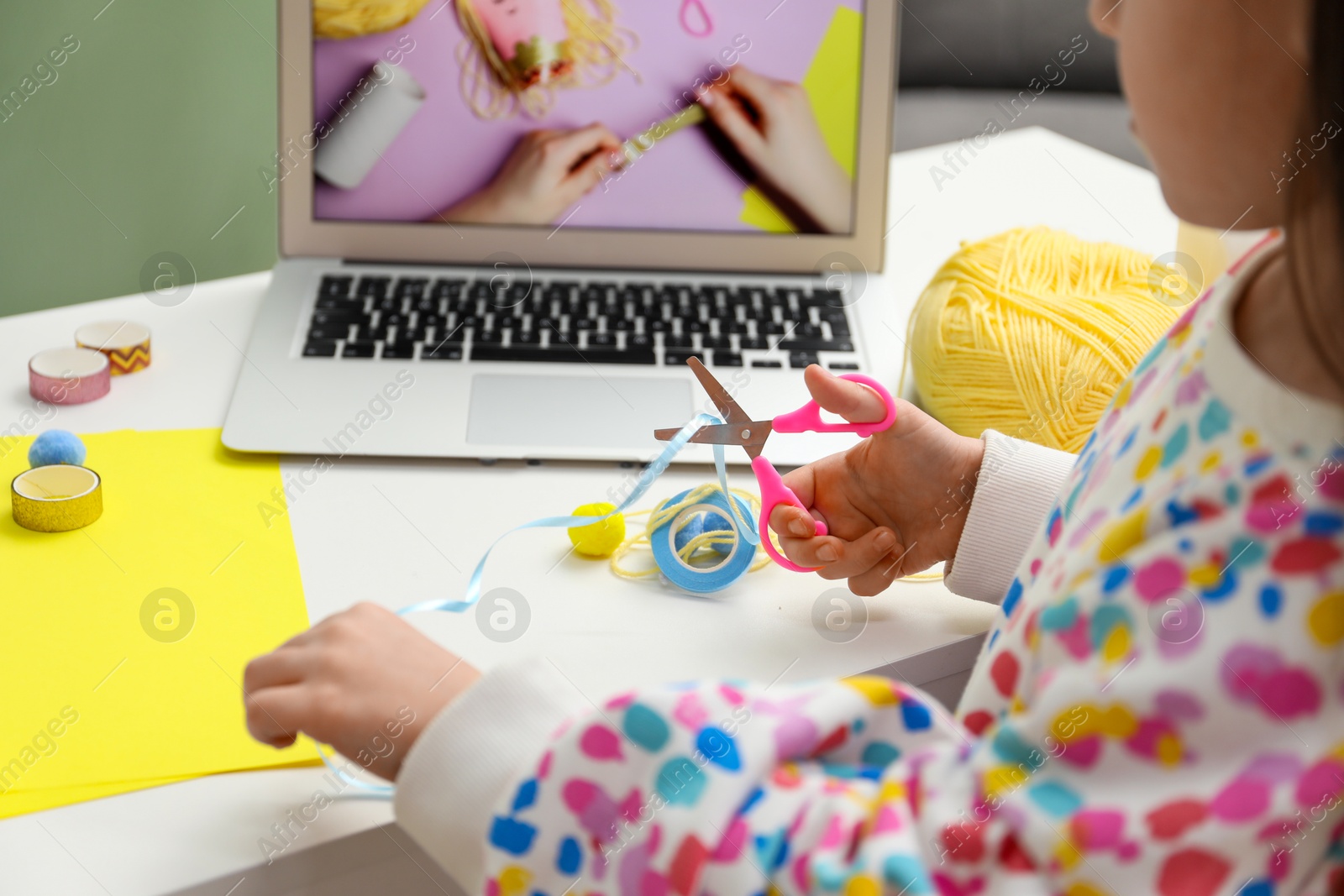 Photo of Little girl making handmade toy by following craft tutorial video at home, closeup. Child creativity