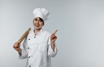 Professional chef with rolling pin pointing at something on light grey background