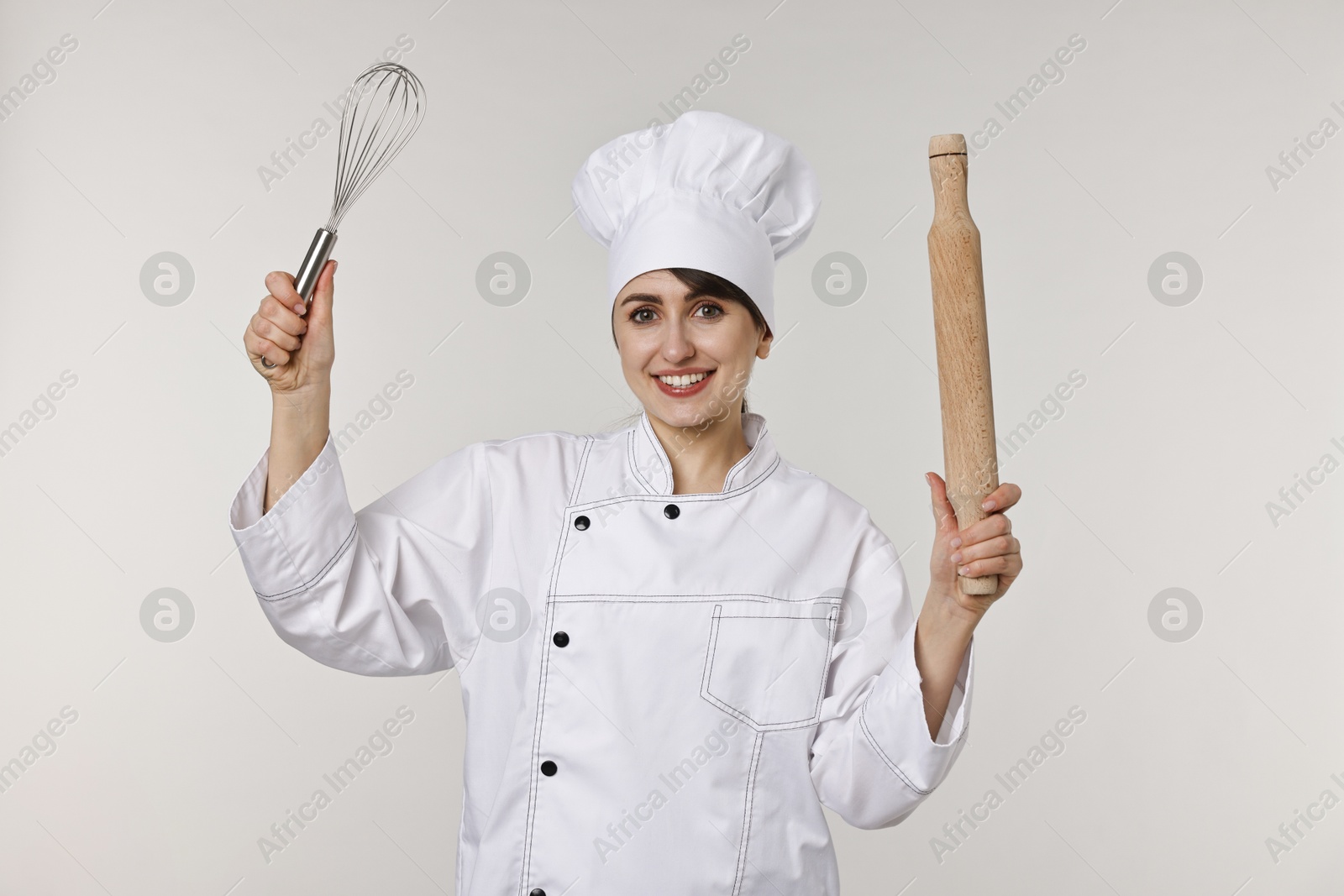 Photo of Professional chef with rolling pin and whisk on light grey background