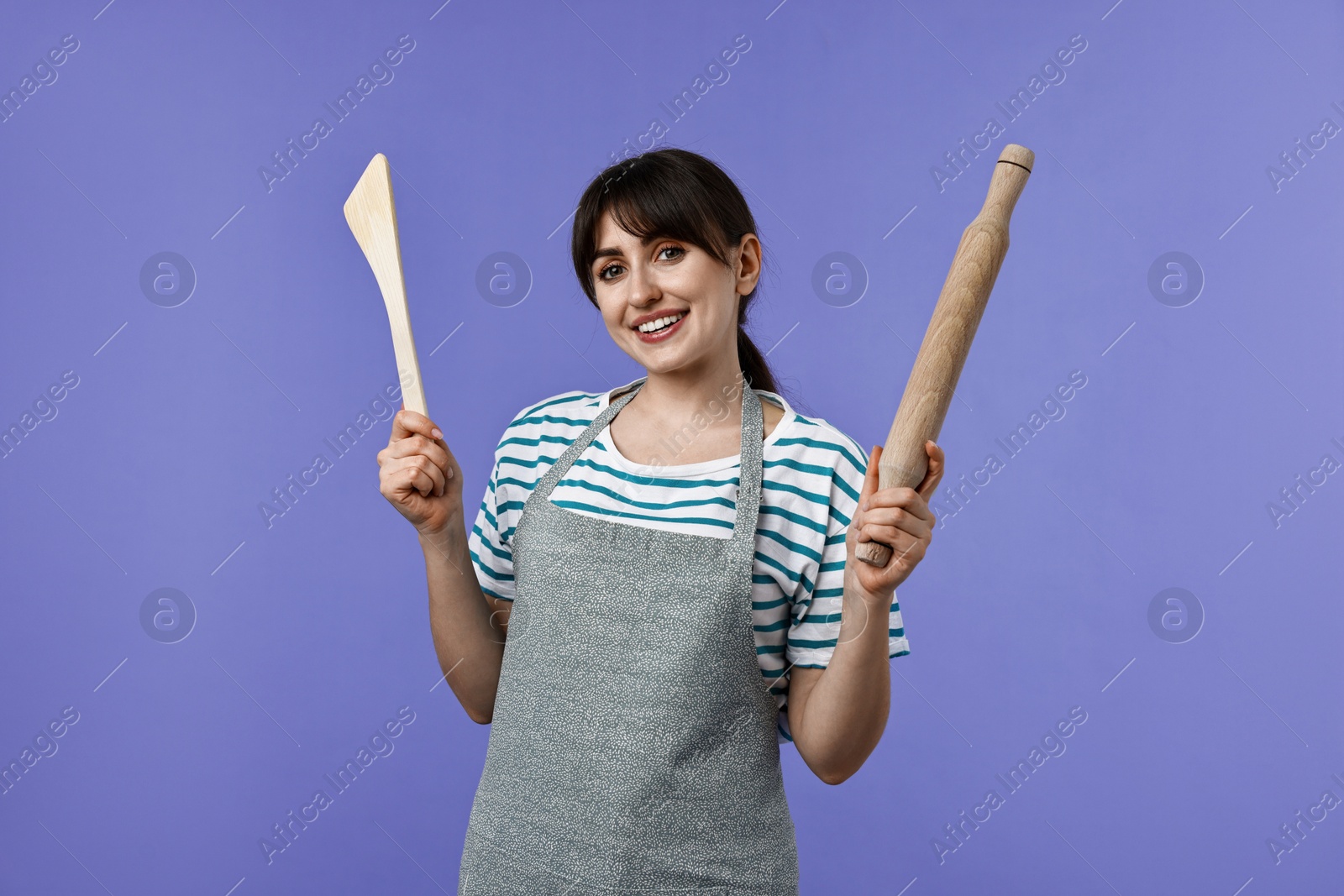 Photo of Happy woman with rolling pin and turner on violet background