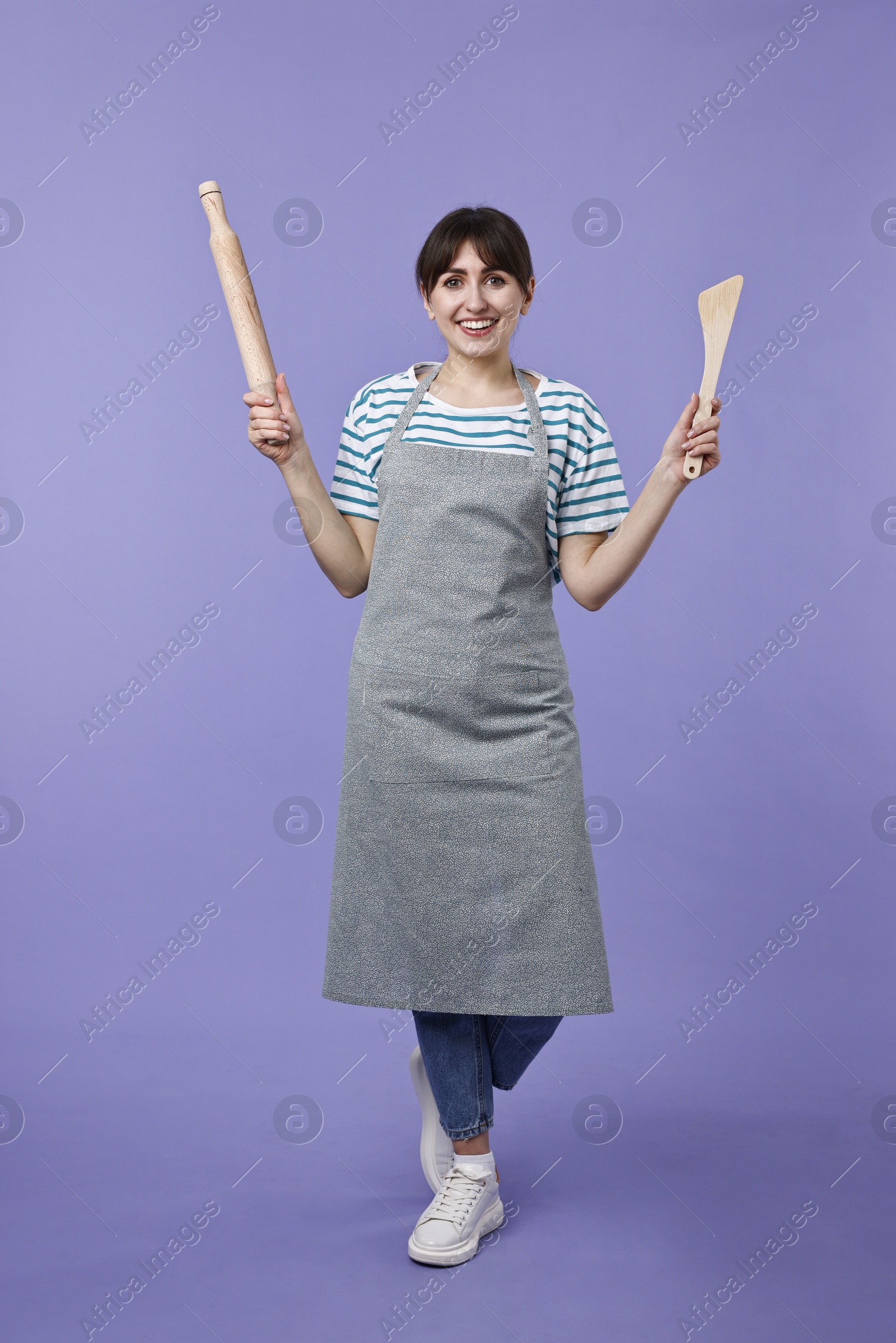 Photo of Woman with rolling pin and turner on violet background