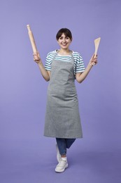 Woman with rolling pin and turner on violet background