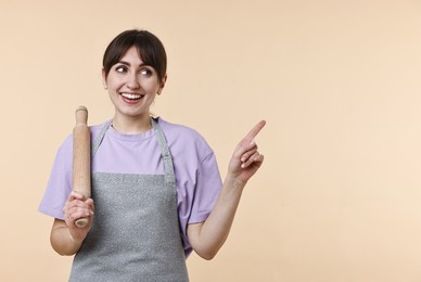 Photo of Woman with rolling pin pointing at something on beige background