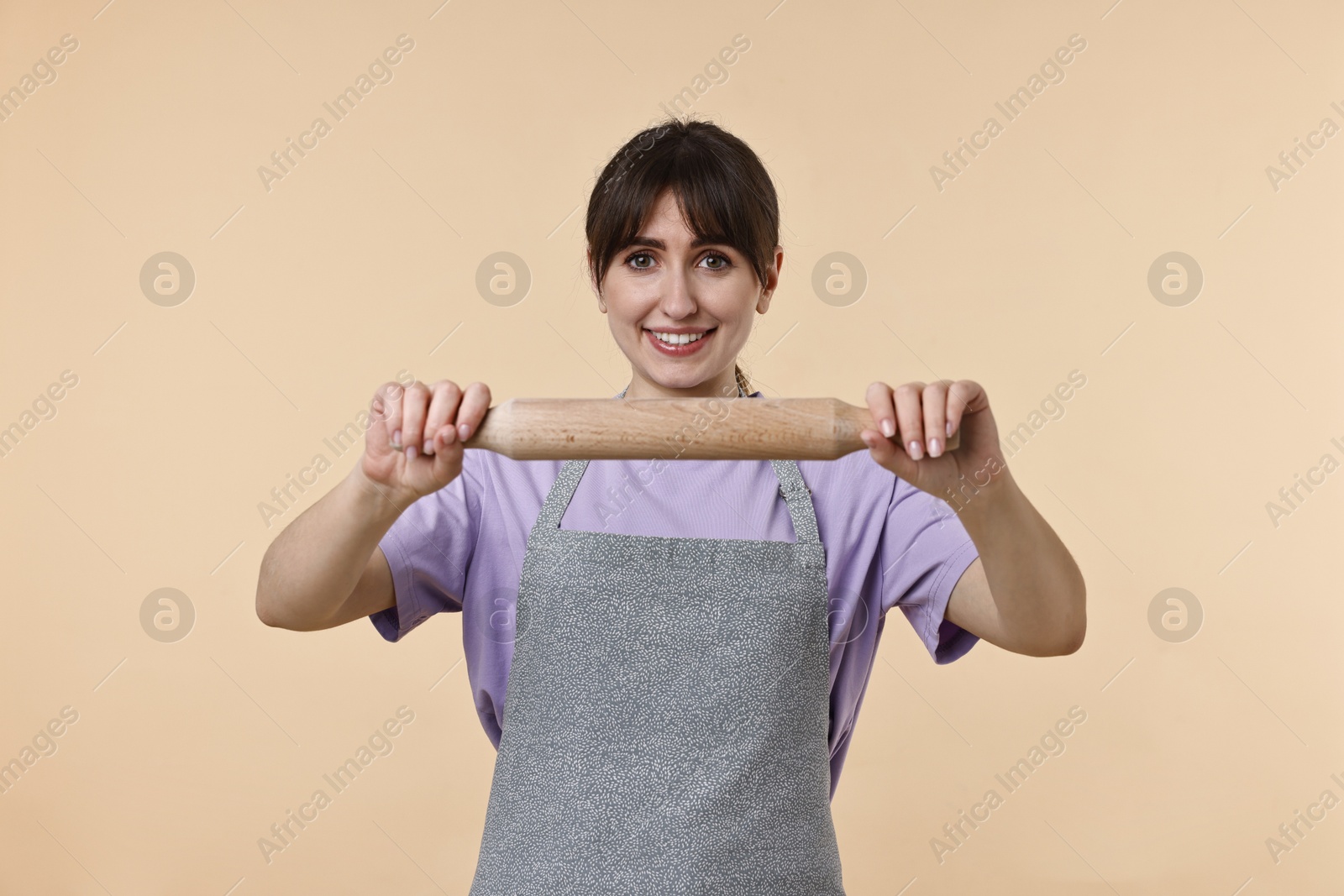 Photo of Happy woman with rolling pin on beige background