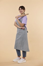 Photo of Happy woman with rolling pin on beige background