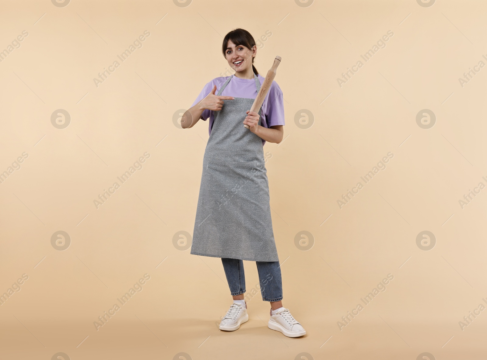 Photo of Woman pointing at rolling pin on beige background