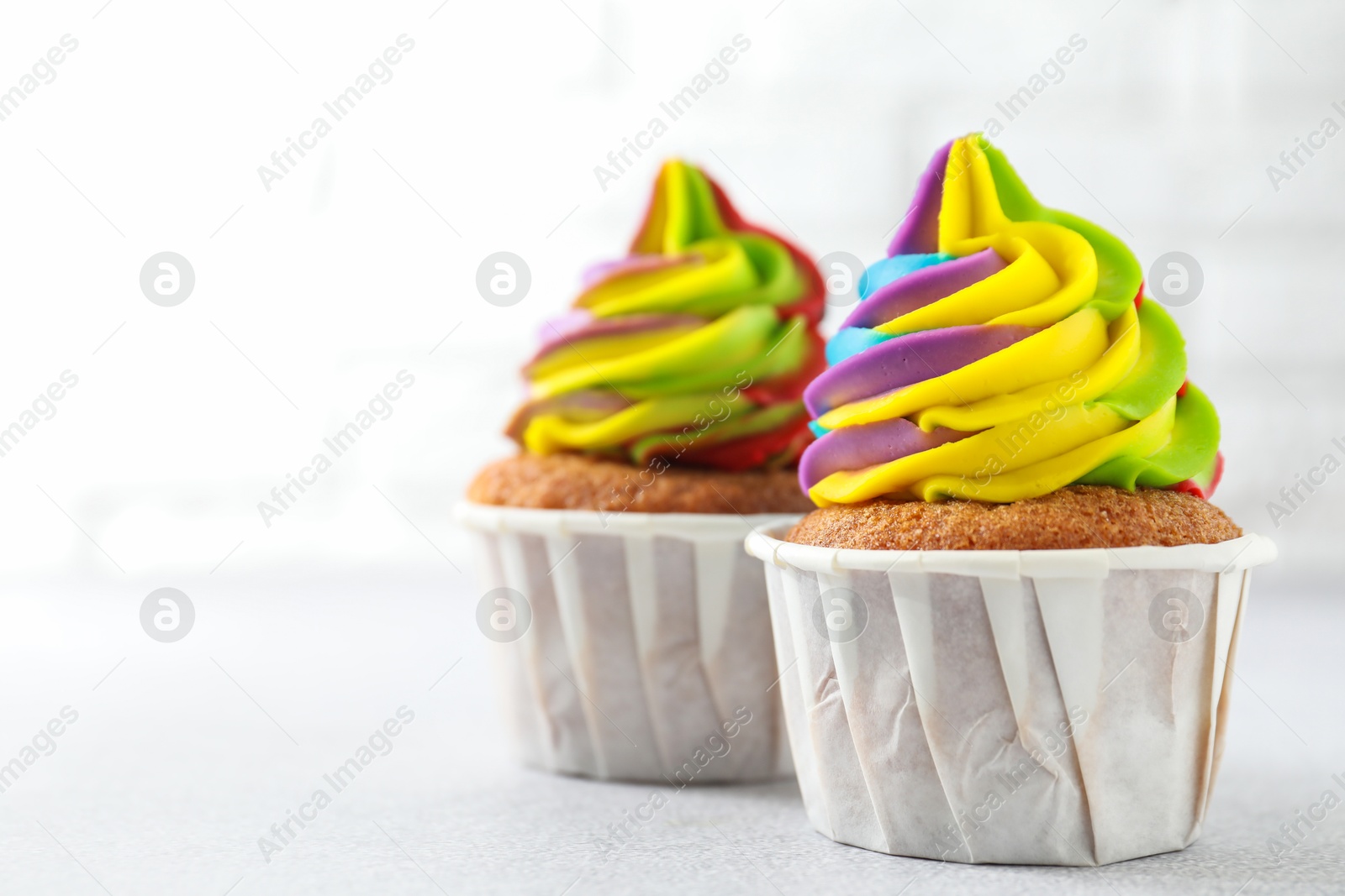 Photo of Tasty cupcakes with colorful cream on white table, closeup. Space for text