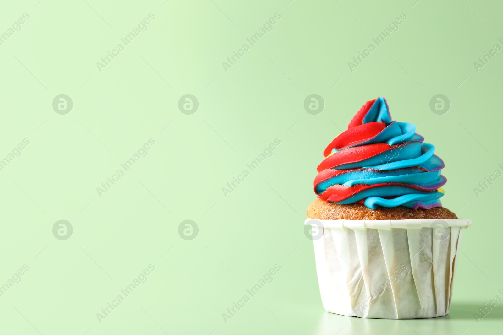 Photo of Tasty cupcake with colorful cream on light green background, closeup. Space for text