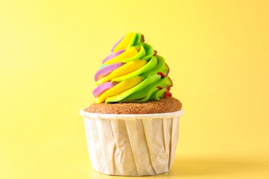 Photo of Tasty cupcake with colorful cream on yellow background, closeup