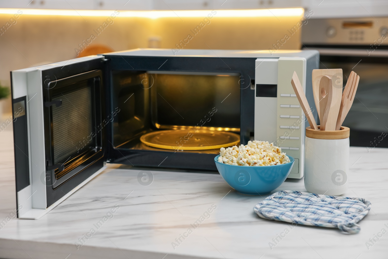 Photo of Tasty popcorn in bowl near microwave oven on white marble table indoors