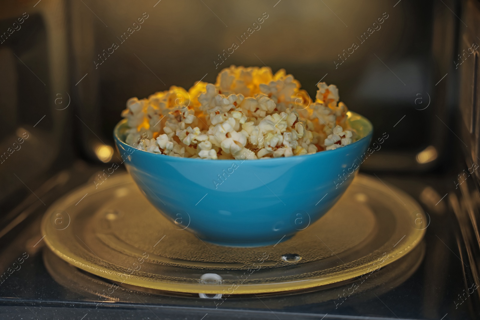 Photo of Bowl of tasty popcorn in microwave oven, closeup