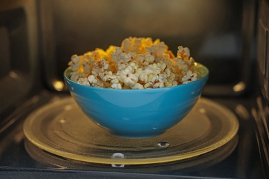 Photo of Bowl of tasty popcorn in microwave oven, closeup