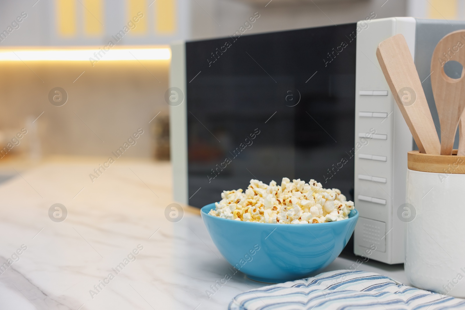 Photo of Tasty popcorn in bowl near microwave oven on white marble table indoors, space for text