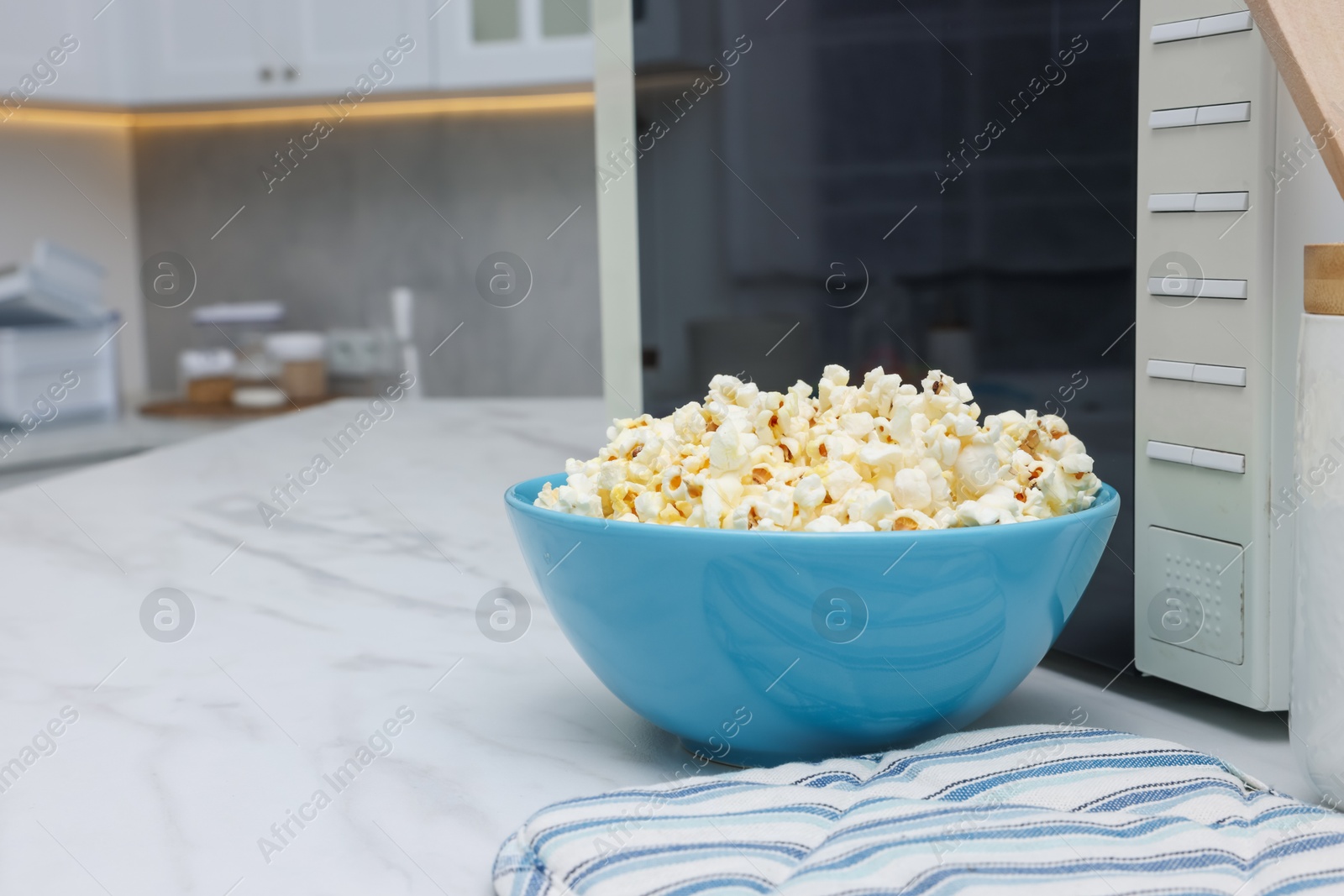 Photo of Tasty popcorn in bowl near microwave oven on white marble table indoors, space for text