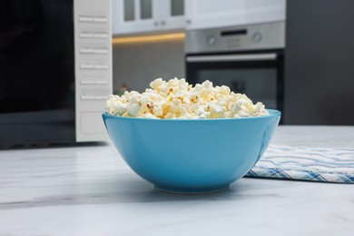 Photo of Tasty popcorn in bowl near microwave oven on white marble table indoors