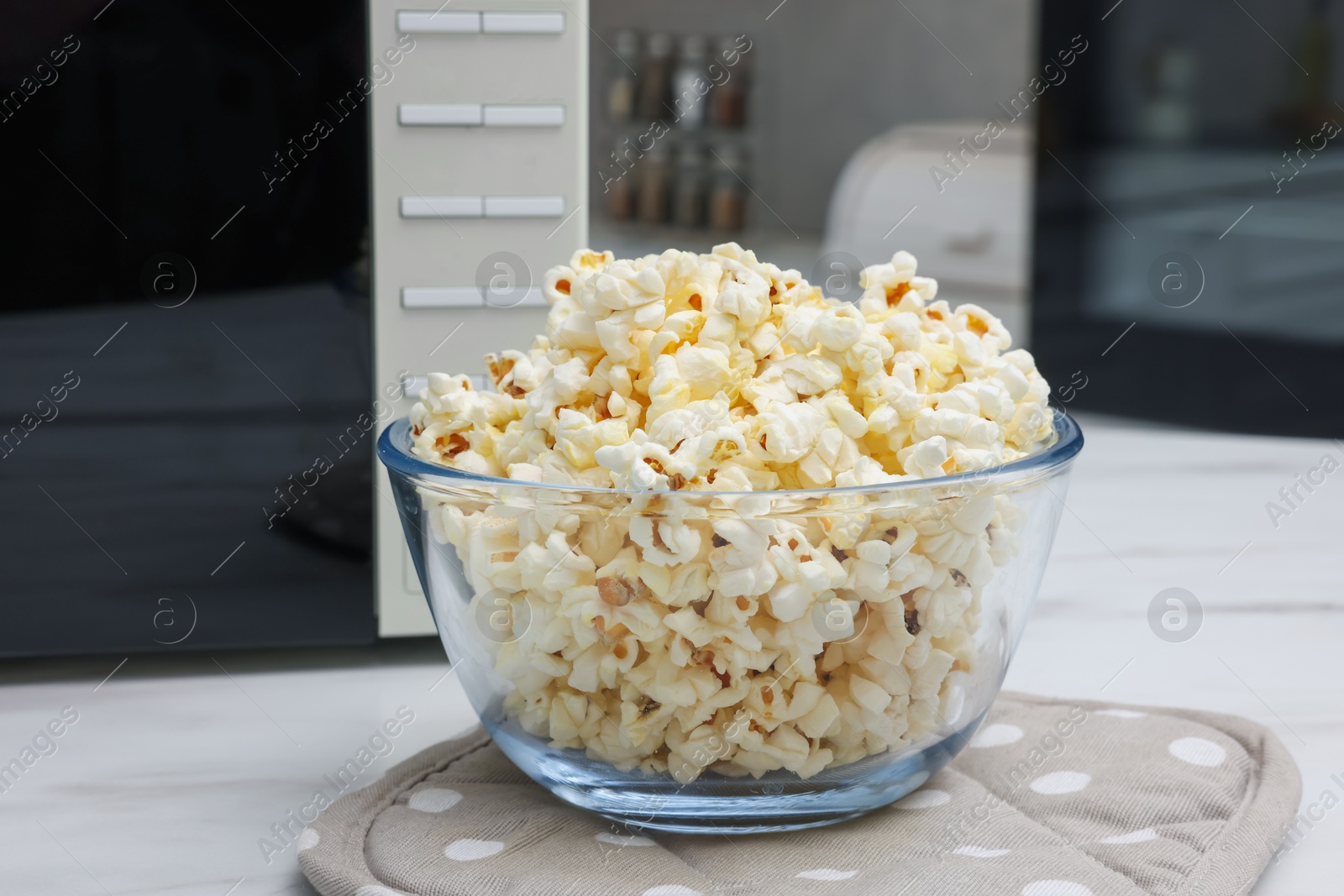 Photo of Tasty popcorn in bowl near microwave oven on white marble table indoors