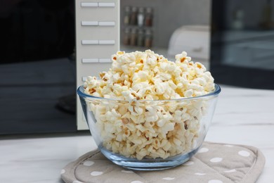 Photo of Tasty popcorn in bowl near microwave oven on white marble table indoors