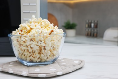 Photo of Tasty popcorn in bowl near microwave oven on white marble table indoors, space for text